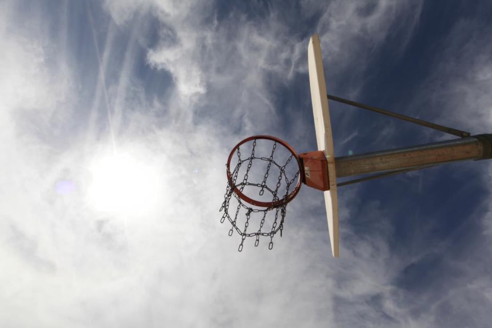 An outdoor basketball hoop with a chain net against a bright sky